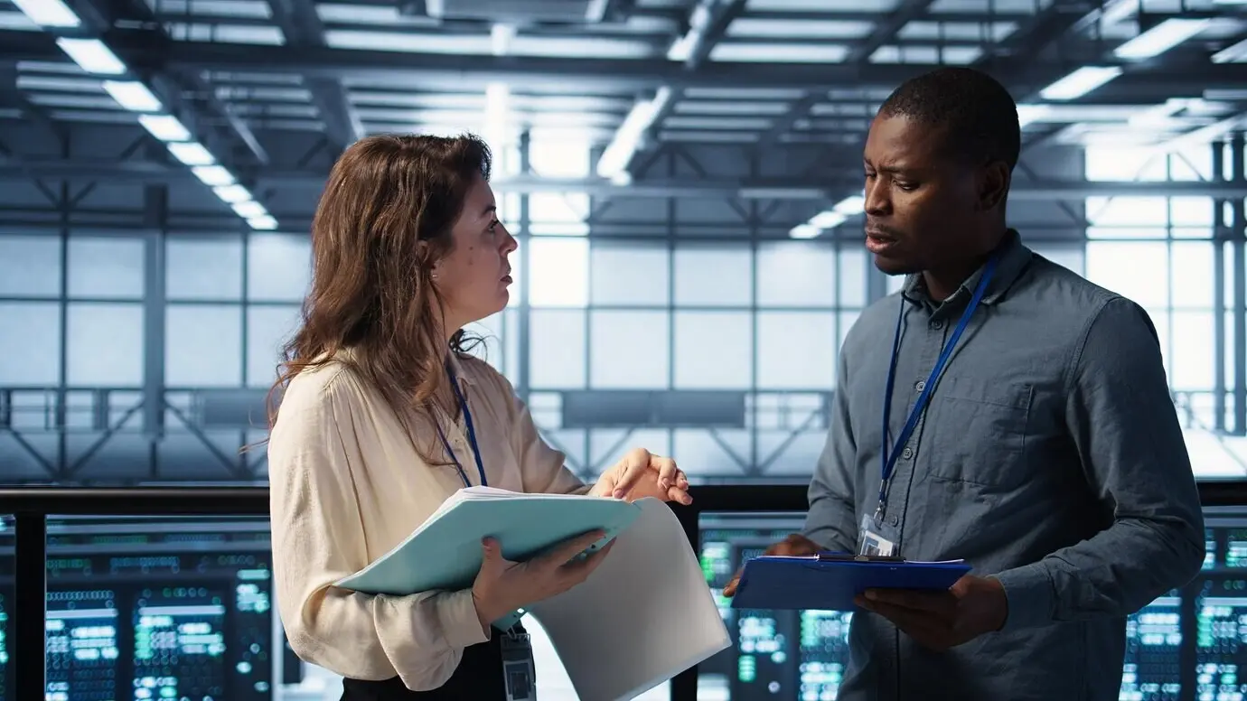 Радостные администраторы встречаются в дата-центре, чтобы просмотреть отчёты, и жмут друг другу руки.