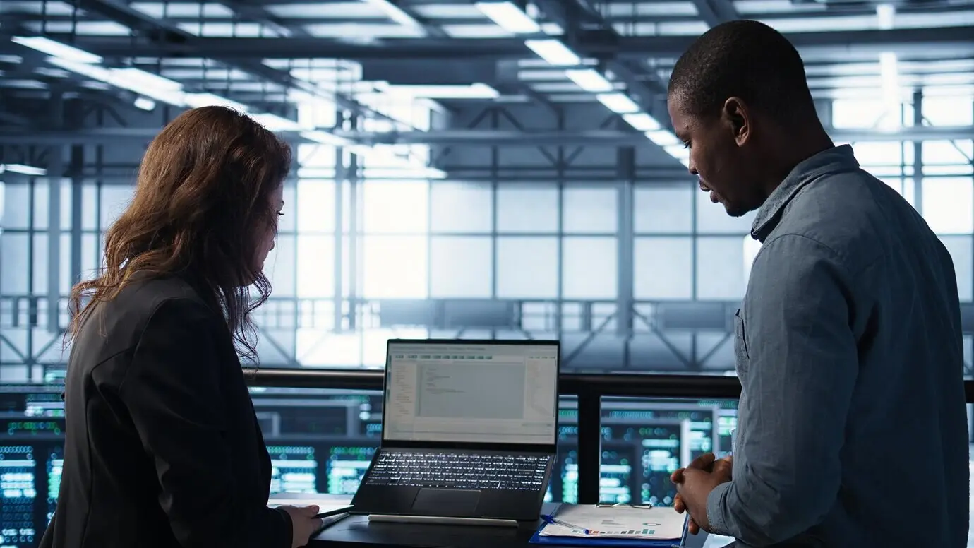 Сотрудники в серверной, использующие искусственный интеллект на ноутбуке и планшете.